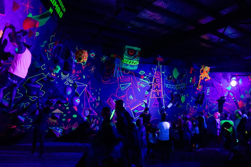 Climbers on a neon-lit indoor climbing wall during a blacklight glow event at Core Climbing